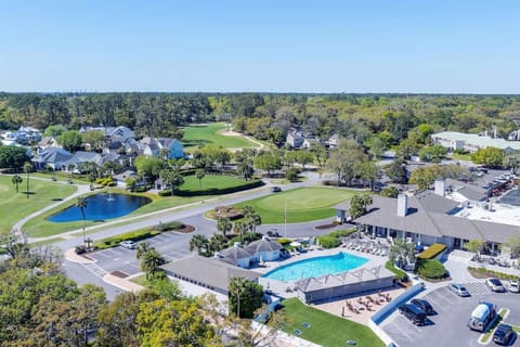 Wide aerial of pool, clubhouse, golf course, and nearby homes