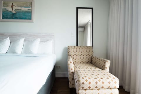 Soft bed and patterned lounge chair near tall mirror