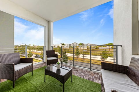 Spacious covered balcony with wicker lounge seating, faux-grass rug, and open community views-perfect for morning coffee or sunset chats.