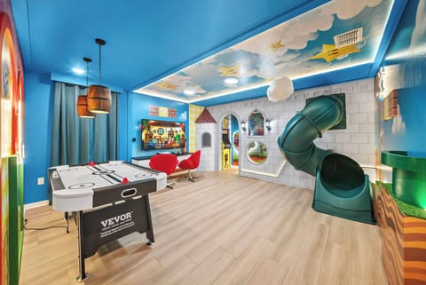Enjoy fun and excitement in our vibrant game room, featuring playful blue walls and colorful accents. With a foosball table and a whimsical slide, it's a charming space where soft lighting creates a cozy atmosphere for everyone.