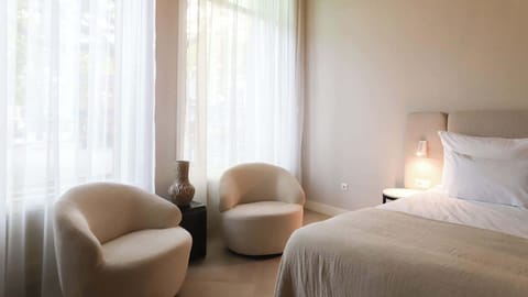 Bright and elegant room with soft neutral tones, rounded lounge chairs and a plush bed for ultimate comfort.