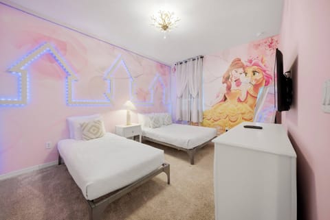 This vibrant bedroom features soft pink walls with enchanting murals and cozy twin beds in sleek metal frames. A charming chandelier adds warmth, making it a delightful retreat for guests seeking a whimsical escape.