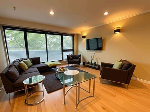 Spacious and modern living room with large windows, comfortable seating, wooden floors, and a wall-mounted TV perfect for relaxing or socialising in a bright, stylish setting.