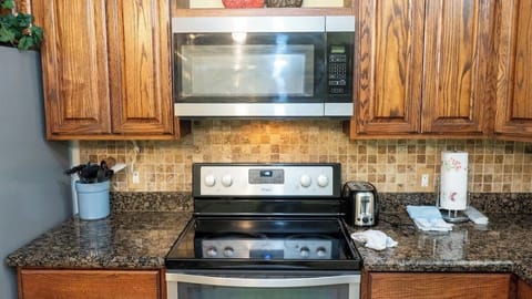 This fully equipped kitchen features a sleek Whirlpool electric stove and stainless steel microwave, complemented by granite countertops and warm wood cabinetry. Convenient small appliances and essentials make meal prep simple and enjoyable.