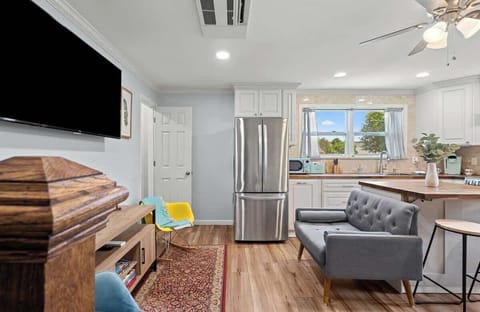 Bright living room w/ sofa seating, wall-mounted TV & large windows bringing in natural light