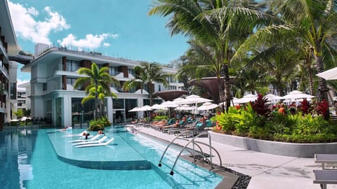 Beautiful resort-style swimming pool with landscaped walkways, tropical greenery, and modern residential buildings.