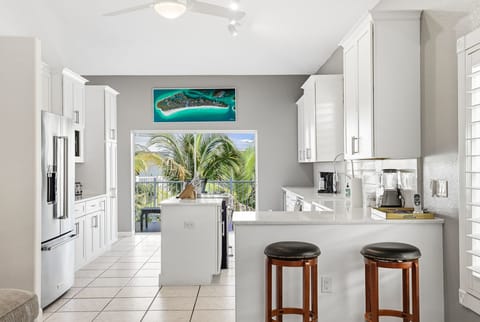 Your spacious kitchen features pristine white cabinetry, modern appliances, and a convenient breakfast bar where you can enjoy your morning coffee while palm trees sway outside.