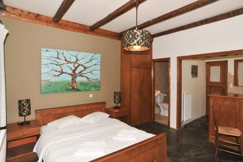 Elegant bedroom with exposed wooden beams, a comfortable double bed, and an en-suite bathroom, combining traditional charm with comfort for a relaxing mountain stay near Lake Doxa.