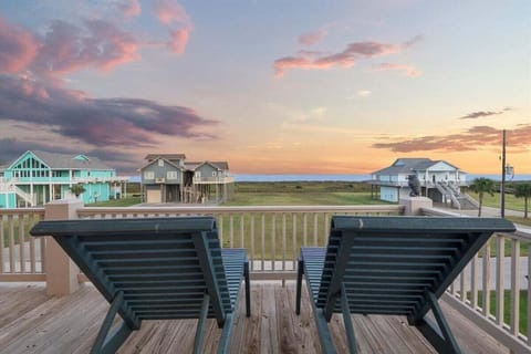 Private deck seating with two lounge chairs overlooking Bolivar Peninsula beach homes, open coastal landscape, and sunset sky near the Gulf Coast.