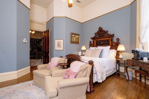 The Eliza Suite bedroom featuring a king bed, antique wood headboard, and a comfortable seating area.