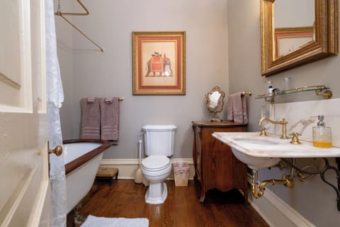 Private bathroom with clawfoot tub, brass fixtures, stone sink, and antique cabinetry.