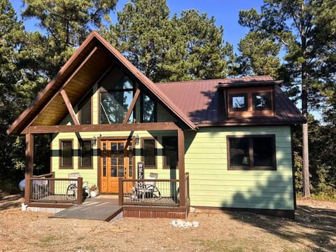 Charming cabin nestled among tall pines with covered porch featuring rocking chairs and mountain-style architecture.