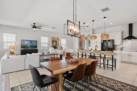 Bright open-concept dining and kitchen area with a large wood dining table, modern lighting, and spacious island seating