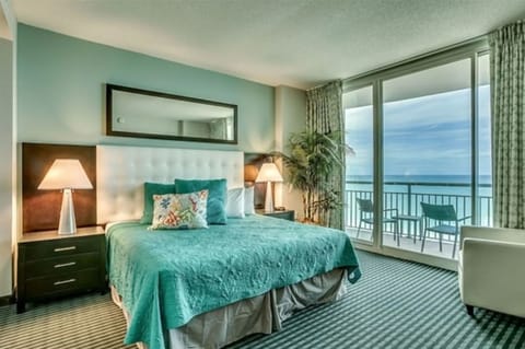 Elegant bedroom with teal bedspread, warm lights, and ocean-view balcony.