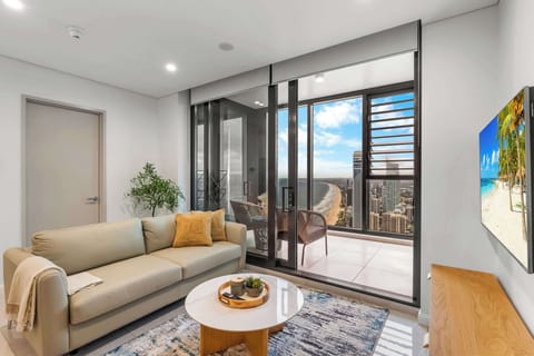Bright living area with premium Nick Scali sofa bed, smart TV, and stunning ocean views stretching along the coastline.