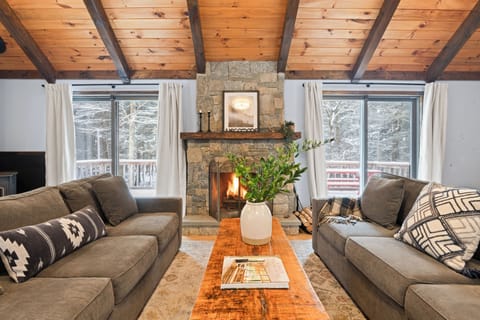 Cozy mountain living room with a stone fireplace, vaulted wood ceilings, and serene forest views.