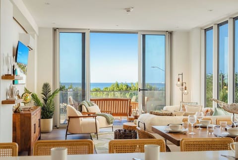 Bright, airy living and dining space with floor-to-ceiling windows framing stunning sea views. Relax in your coastal retreat filled with natural light and modern coastal charm.