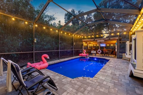 This well-designed pool area includes a spacious deck, cozy seating, and a beautiful natural backdrop behind the screened enclosure.