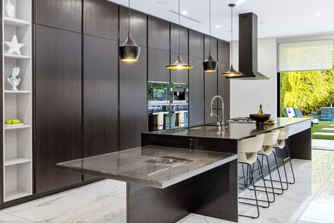 Sleek chef’s kitchen with waterfall island, custom cabinetry, statement pendants, and seamless indoor-outdoor flow for elevated entertaining.