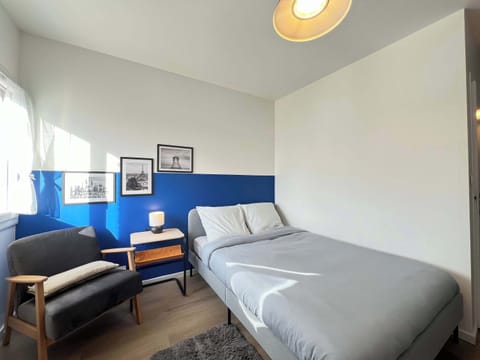 Vue d'ensemble du studio L'Azur — lit double, fauteuil et mur bleu cobalt dans le quartier Cartoucherie à Toulouse