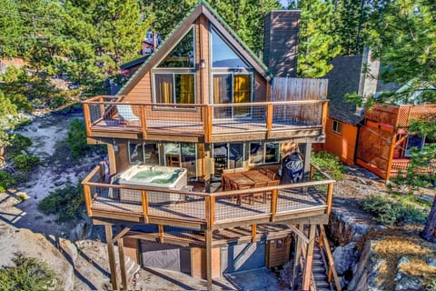 Modern A-frame cabin features multiple decks, hot tub, and contemporary design nestled among mature trees in a peaceful neighborhood setting.