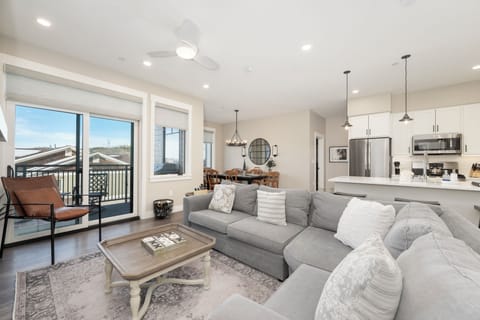 Relax in your stylish open-concept living space with plush gray sectional, modern kitchen, and bright mountain views through expansive windows.