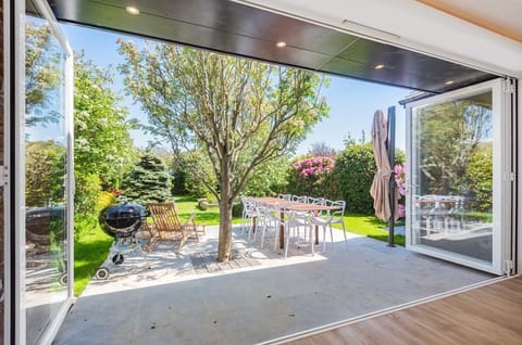 Full-width bi-fold doors open out onto a lovely garden with lush greenery, small lawn for the kids to play and a large patio space