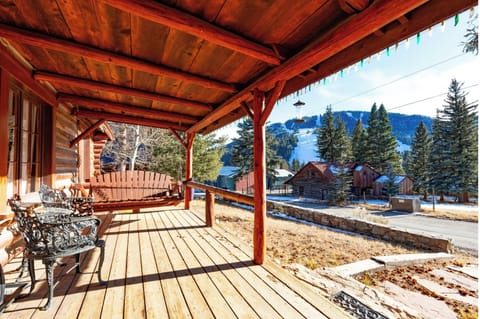 Charming covered porch framed by rustic timber beams in a scenic mountain community, featuring a cozy porch swing overlooking wooded slopes, neighboring cabins, and peaceful residential surroundings.