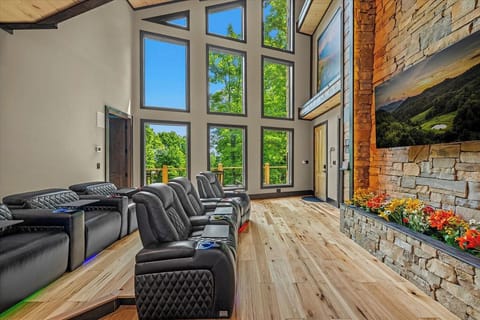 Unwind in this stunning living room, where towering windows flood the space with natural light and frame lush summer treetops. Sink into plush recliners facing the stone fireplace, where warmth and mountain views create your perfect retreat.