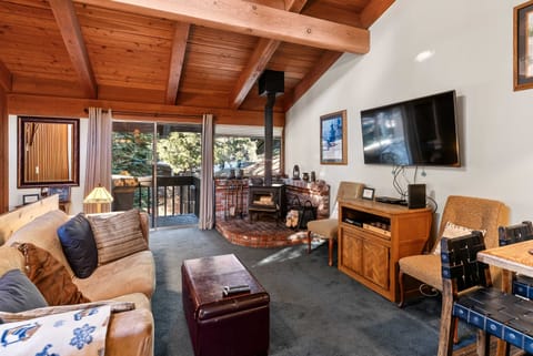 Open living area with vaulted wood ceilings, a cozy wooden fireplace, and a private balcony.