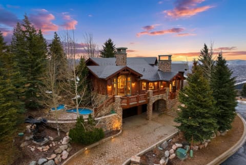 Exterior lodge view at sunset:
Exterior view of a luxury mountain lodge at sunset, featuring timber construction, stone details, warm interior lighting, and surrounding evergreen trees.