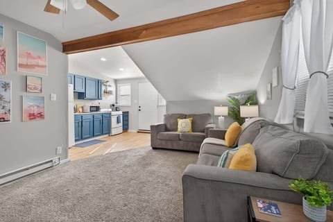 The cozy living room features sloped ceilings with wooden beams and soft neutral decor. Warm lighting and comfortable seating create an inviting space to unwind. 