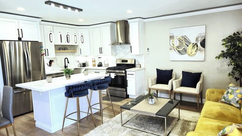 Modern open‑plan kitchen and living room with white cabinetry, kitchen island, yellow sofa, accent chairs, wooden flooring, and contemporary decor.