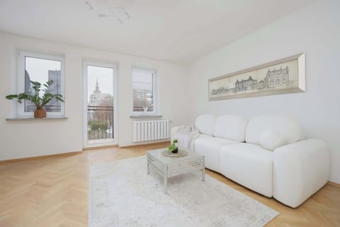 A bright living room with a white sofa, coffee table, and wall art, creating a cozy and inviting space. Large windows allow natural light to fill the room.