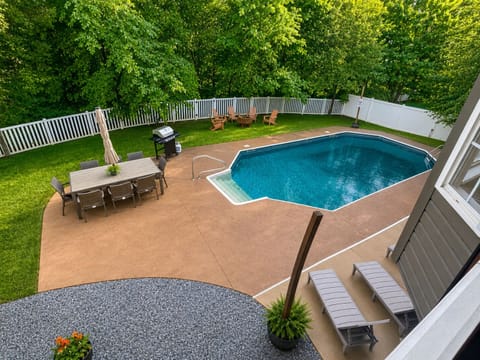 The fenced backyard centers on a large in-ground pool with dining, grilling, loungers, and a firepit seating area.