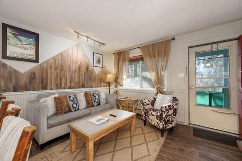 Relax in your cozy alpine-inspired living room with rustic wood accents, plush seating, and charming curtains framing natural light.