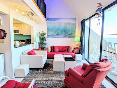 908 Dover Sea Colony East Great Room - Bright, multi-level living room at 908 Dover with bold red seating and floor-to-ceiling glass doors opening to ocean views.