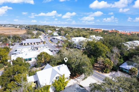 Aerial view of a charming white coastal property nestled among mature trees in a quiet residential neighborhood near the ocean.