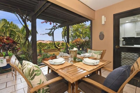 A cozy outdoor dining lanai surrounded by lush tropical landscaping and vibrant garden colors.