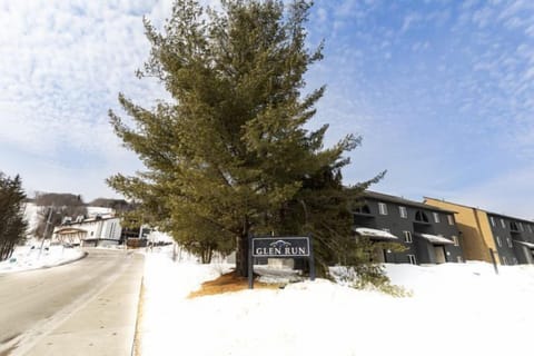The entrance to Glen Run Condos is framed by majestic evergreen trees and a snowy landscape, setting a serene winter scene that invites guests into a cozy mountain retreat.