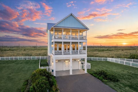 Luxury Gulf-front beach home with elevated design, private driveway parking, and expansive covered balconies overlooking the coastline at sunset.
