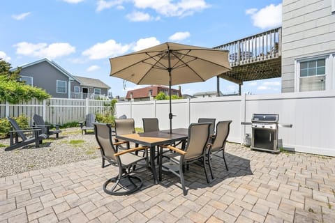 Enjoy outdoor dining and relaxation in this private, paver-stone patio area, featuring a spacious table for six and a large shade umbrella. A modern grill is ready for your next barbecue, perfect for casual meals with family and friends.