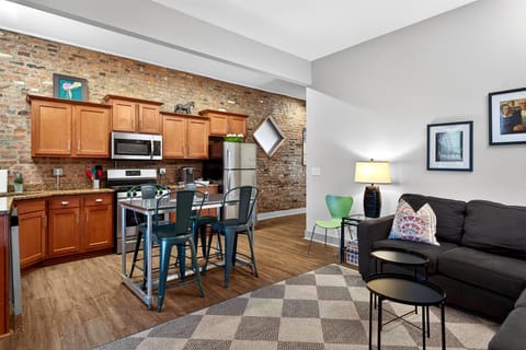 This open concept space features a comfy black sofa with colorful pillows right next to the kitchen island. It is the perfect setup for chatting with the cook while enjoying a drink.