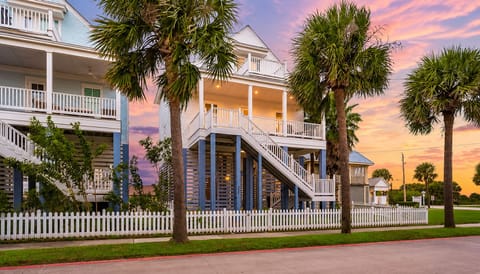 Front exterior view showcasing elevated construction, covered decks, palm-lined surroundings, and convenient access to the coastal neighborhood.