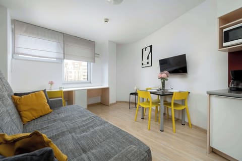 Bright studio with sofa bed, dining table, and natural daylight.