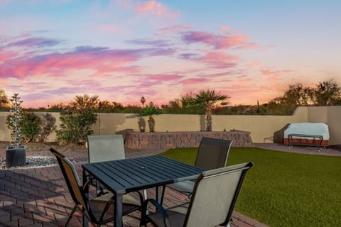 Fully fenced backyard with outdoor dining and seating, gas grill, turf area, and beautiful desert views