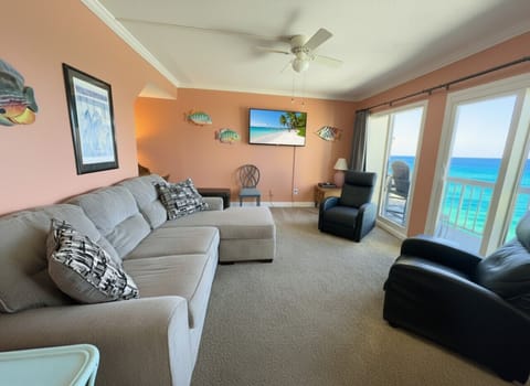 Elegant living room with sectional sofa, recliners, flat-screen TV, and panoramic Gulf views from the private balcony.