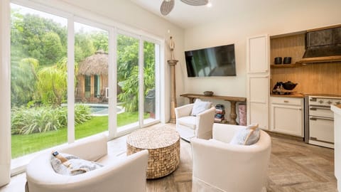 Relax in your stylish living space with garden views, modern kitchen, and tropical palapa glimpses through floor-to-ceiling windows...