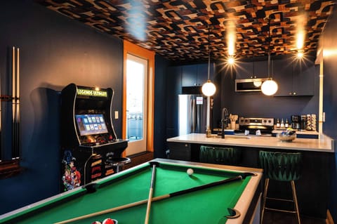Stylish game room with pool table, arcade machine, and a chic kitchenette—perfect for hanging out, grabbing drinks, and enjoying endless fun.