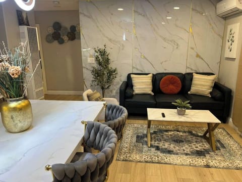 A stylish living room featuring a modern dark sofa, marble‑accent wall panels, chic decor, and a cozy rug. A sleek coffee table, elegant bar seating, and soft lighting create a warm, inviting space in this Spring Valley home.
